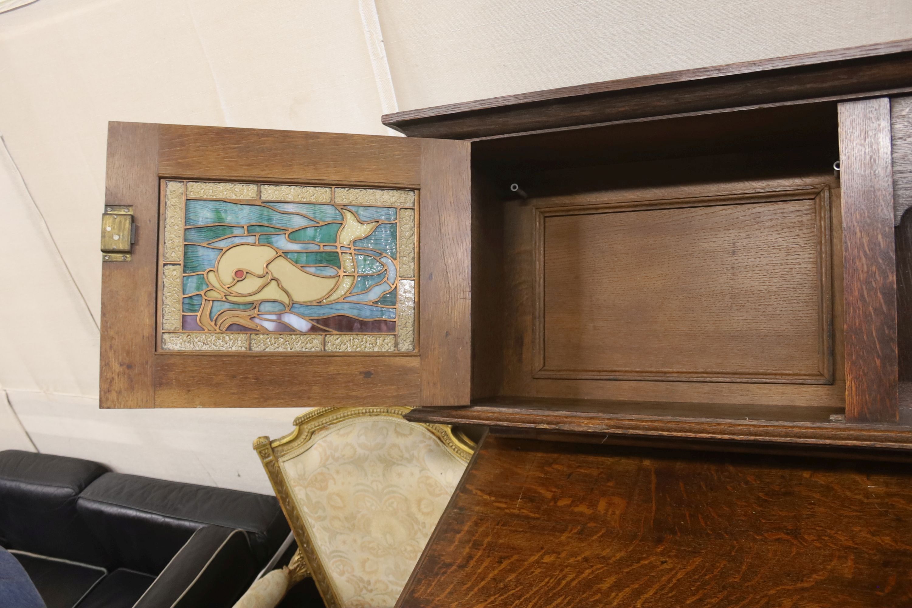 An Arts & Crafts style oak sideboard with stained glass dolphin panels, length 182cm, depth 60cm, height 145cm (lacks top section suppo